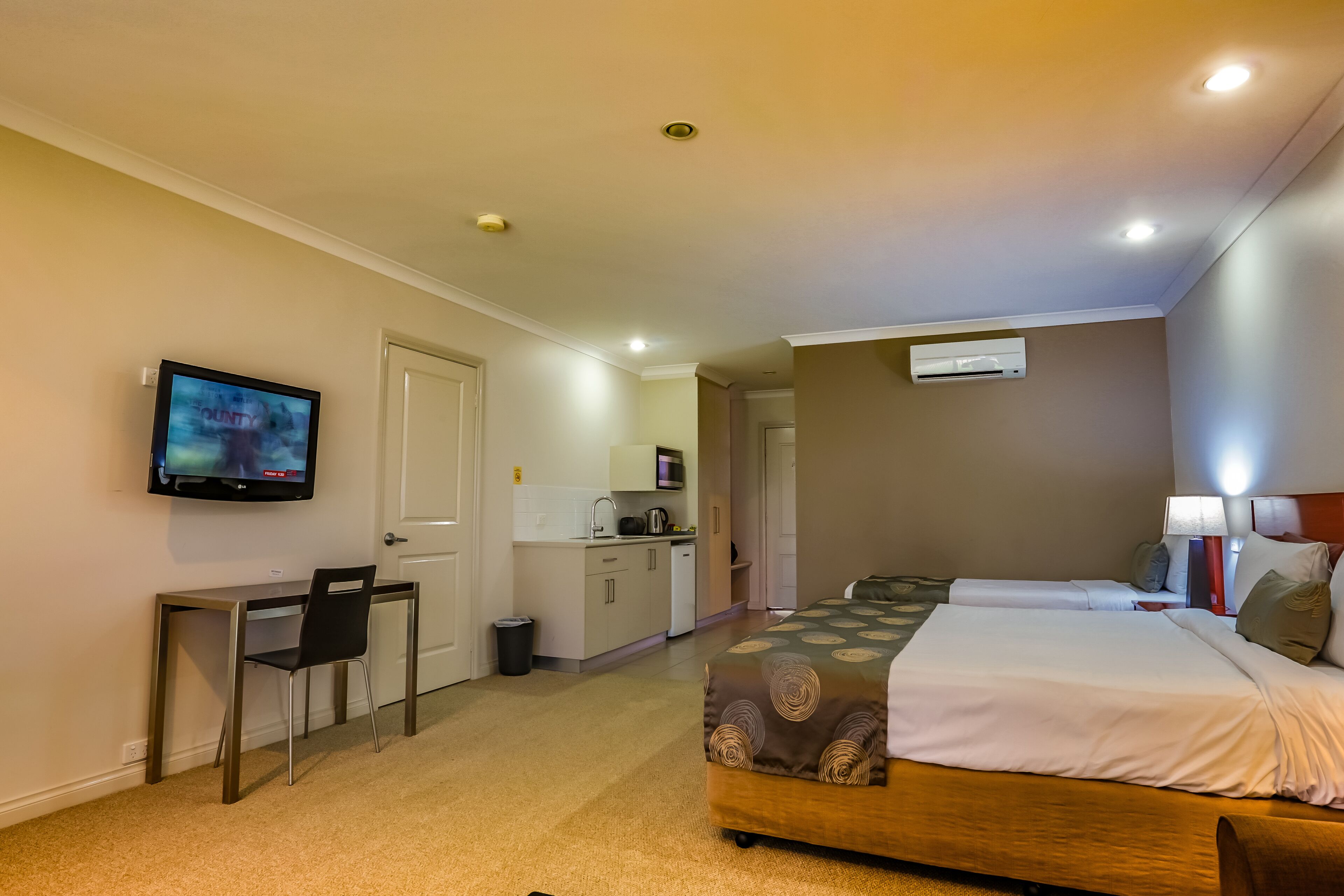 A hotel room with a bed, desk, chair, TV, kitchenette, and a bathroom.