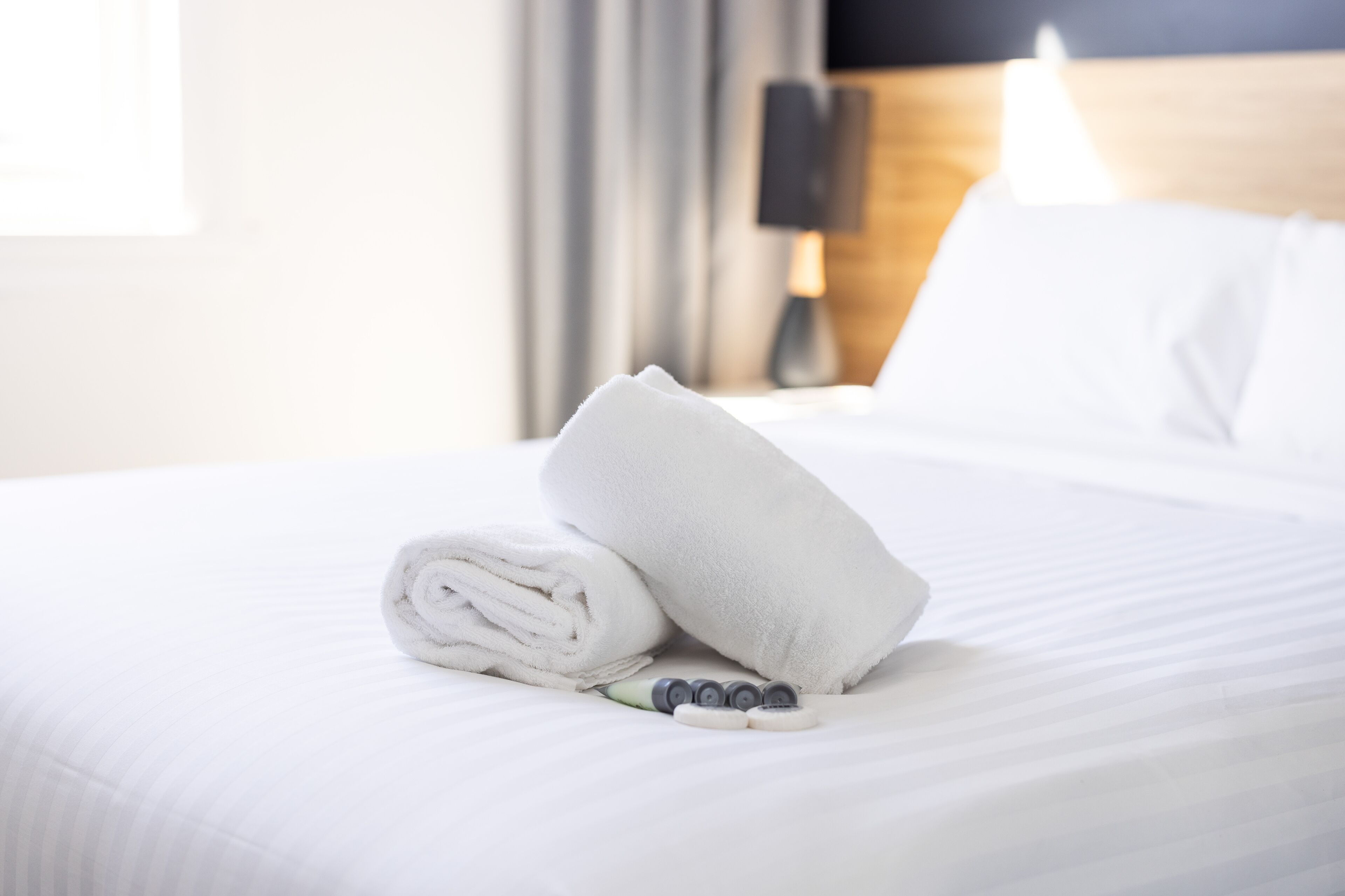 A neatly made bed with a rolled towel, a pillow, and a set of toiletries.