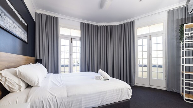 A modern hotel room with a large bed, grey curtains, a white headboard, and a view of the outdoors through the windows. - The Albion Hotel (Wickham)