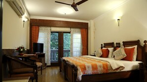 A bedroom with a bed, a desk, a chair, a television, and a window with curtains. - The Estate Villa (New Delhi)