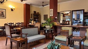 A spacious lobby with a dining area, a bar, and a seating area with wooden furniture and plants. - The Estate Villa (New Delhi)