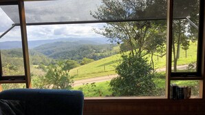 A room with a large window offering a view of a green valley and hills. - Top Cottage at Maleny (Wootha)