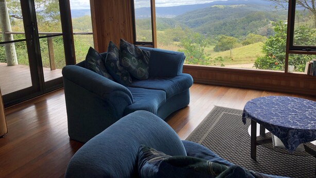 A room with a blue sofa, a small round table, and large windows offering a view of a mountainous landscape. - Top Cottage at Maleny (Wootha)