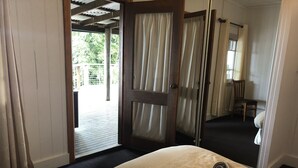 A hotel room with a bed, a wooden door leading to an outdoor area, and a mirror reflecting the room. - Top Cottage at Maleny (Wootha)
