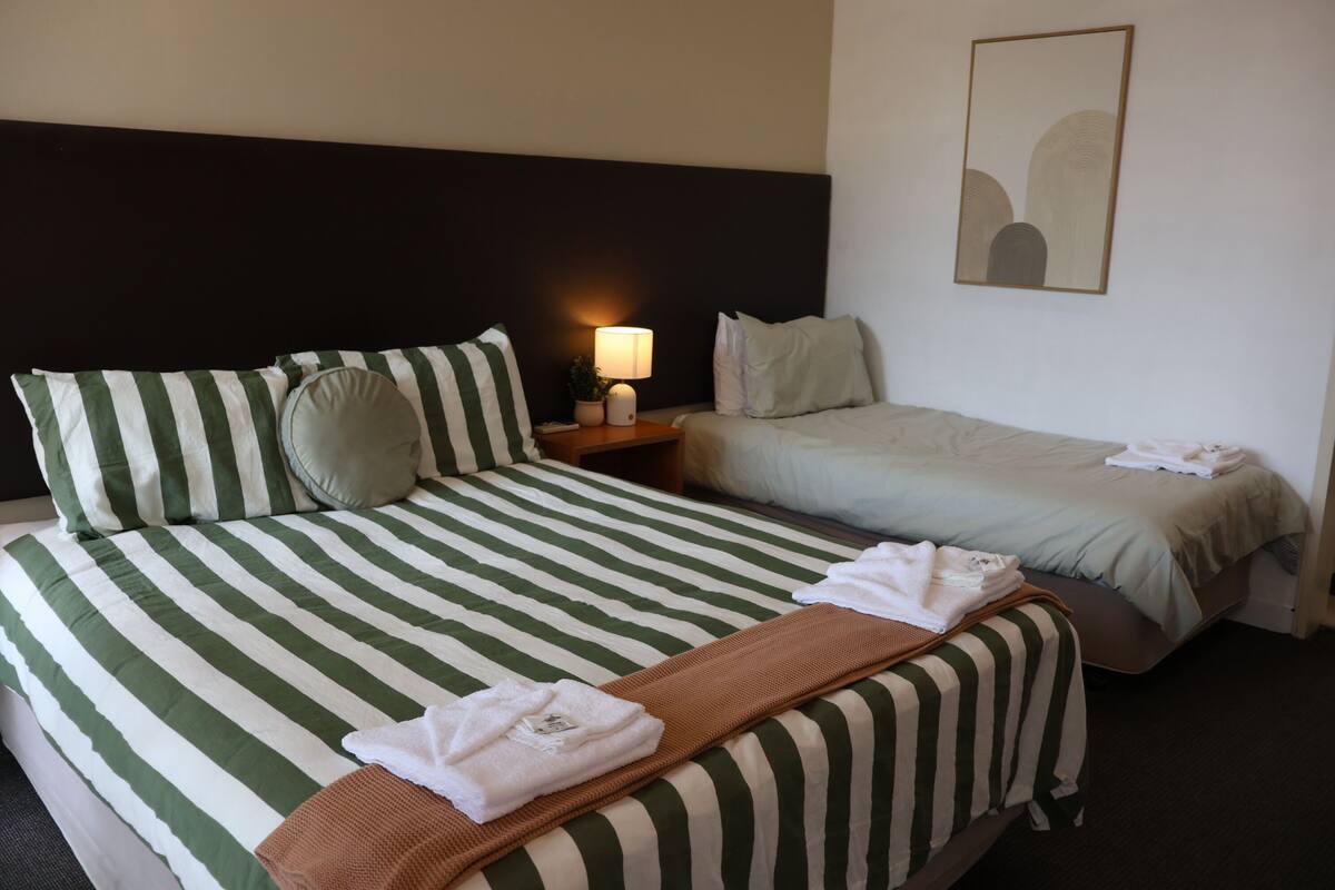 A hotel room with two beds, a nightstand with a lamp, and a framed picture on the wall.