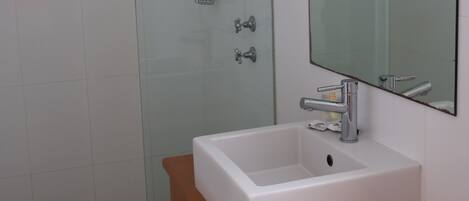 Un baño con cabina de ducha de vidrio, un lavabo blanco y un mueble de tocador de madera.