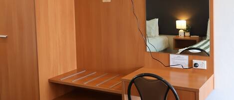 Habitación de hotel con un escritorio de madera, una silla, un televisor de pantalla plana en la pared y una mesita de noche con lámpara.