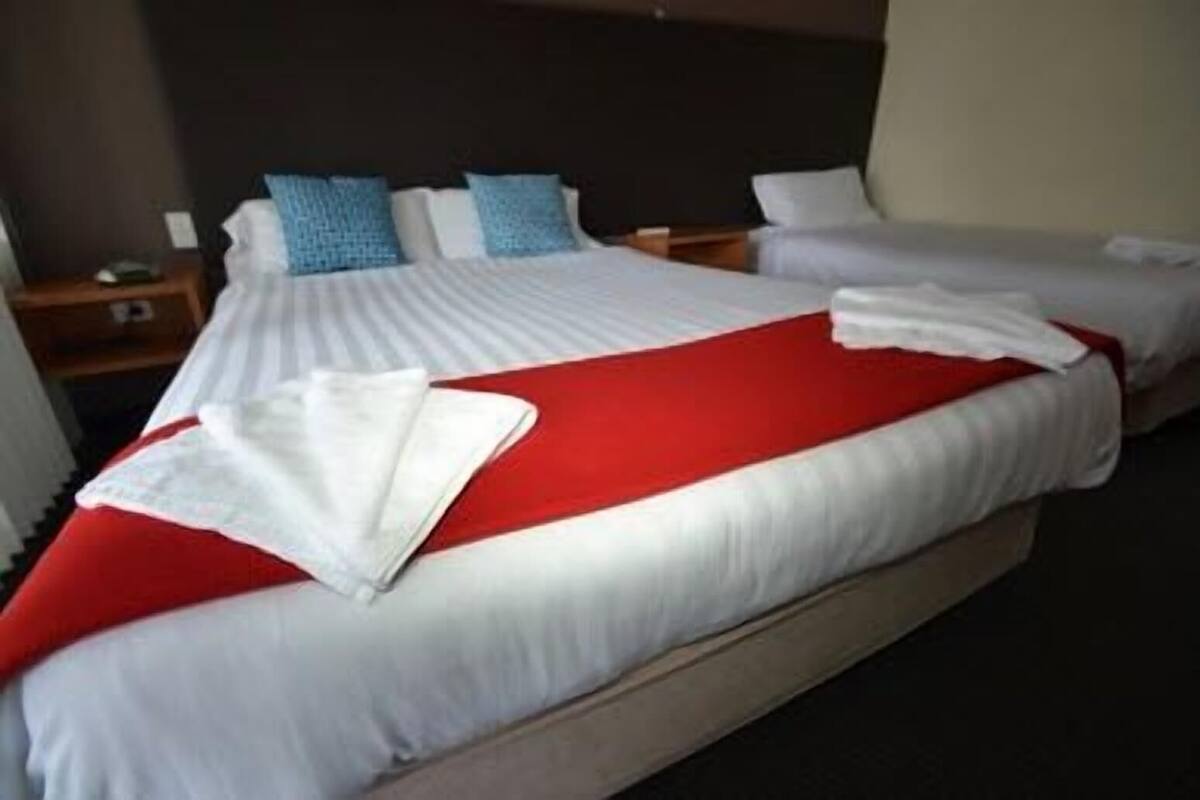 A hotel room with two beds, each with white and red bedding, and a wooden headboard.