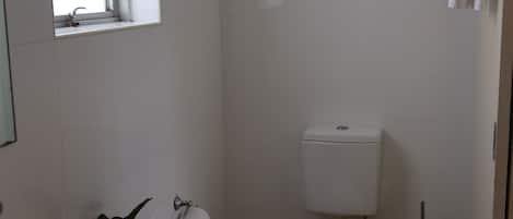 Een kleine, schone badkamer met een wit toilet, een wastafel en een raam.