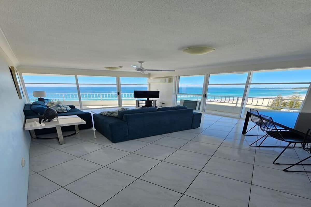 Un vaste espace de vie avec une grande fenêtre donnant sur la plage, un ventilateur de plafond et un téléviseur à écran plat.