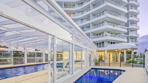 Ett modernt hotell med poolområde, balkonger med glasväggar och en väl upplyst entré.