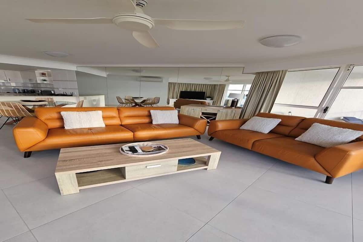 Un salon moderne avec deux canapés en cuir orange, une table basse en bois et un ventilateur de plafond.
