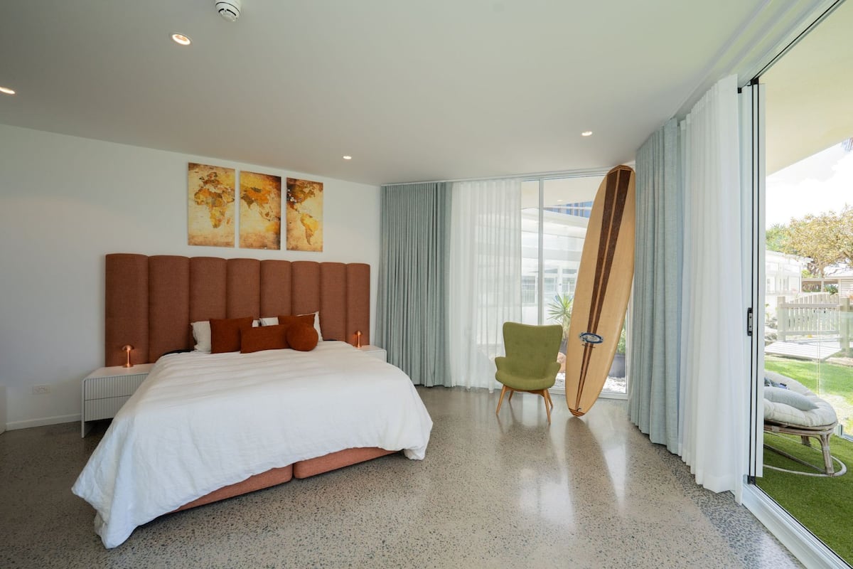 Une chambre d’hôtel moderne avec un grand lit, un fauteuil vert et une vue sur l’extérieur.