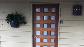 A wooden door with a grid pattern and frosted glass panels, flanked by a potted plant with purple flowers and a wicker basket on the ground. - Maleny Mountain Retreat (Wootha)