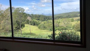 A window with a view of a green landscape, trees, and a distant mountain. - Maleny Mountain Retreat (Wootha)