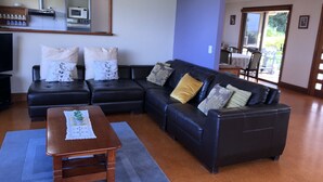 A living room with a sectional sofa, a wooden coffee table, a TV, and a kitchen area with a microwave and stove. - Maleny Mountain Retreat (Wootha)