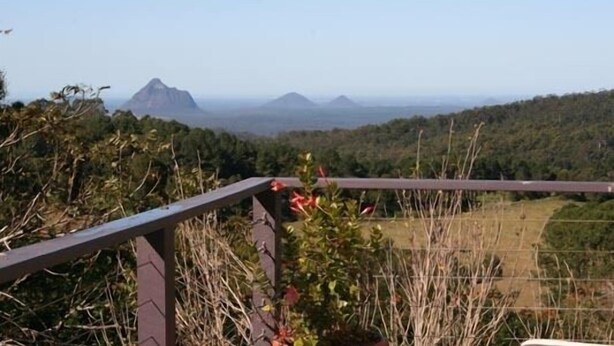 A scenic view from a balcony with a metal railing, overlooking a hilly landscape with distant mountains. - Maleny Mountain Retreat (Wootha)