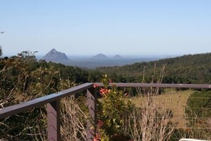 Ein malerischer Ausblick von einem Balkon mit Metallgeländer auf eine hügelige Landschaft und entfernte Berge.
