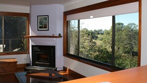 A modern kitchen with a fireplace, large windows, and a view of the surrounding forest. - Maleny Mountain Retreat (Wootha)