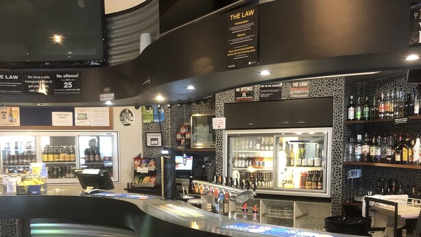 A bar area with a curved counter, shelves with bottles, and a menu board. - Tinwald Motels (Ashburton)