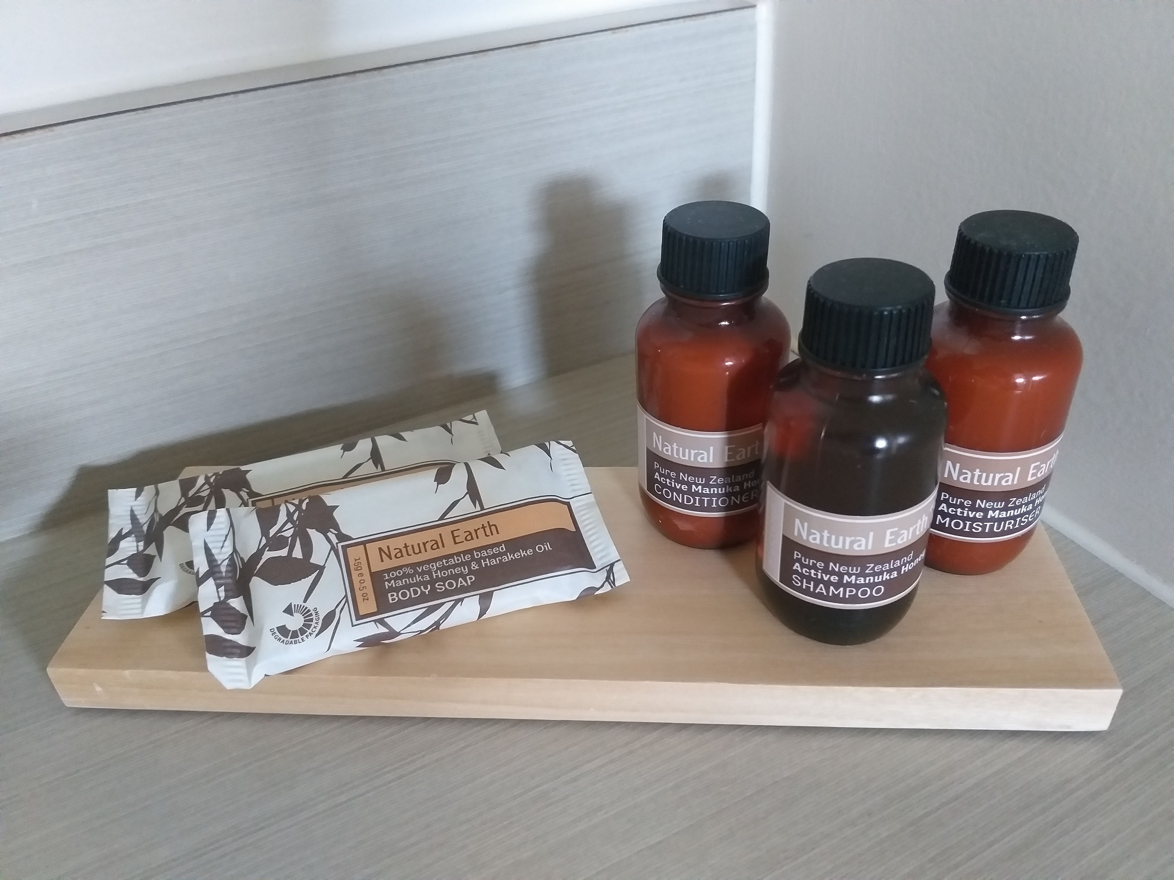 Una bandeja de madera con cuatro botellas de productos corporales Natural Earth y un paquete de jabón.