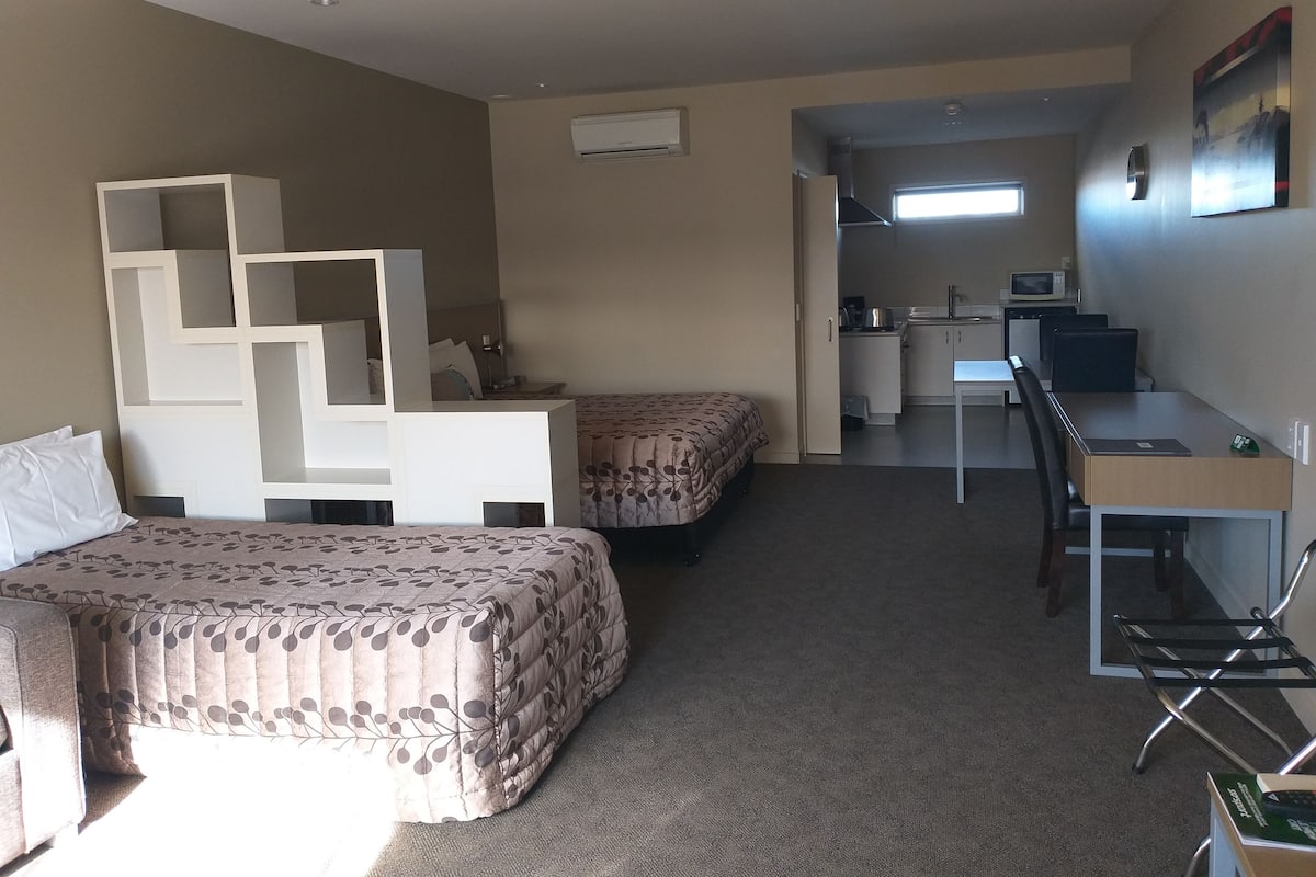 Ein kleines Hotelzimmer mit zwei Betten, einem Schreibtisch und einer Küchenzeile.