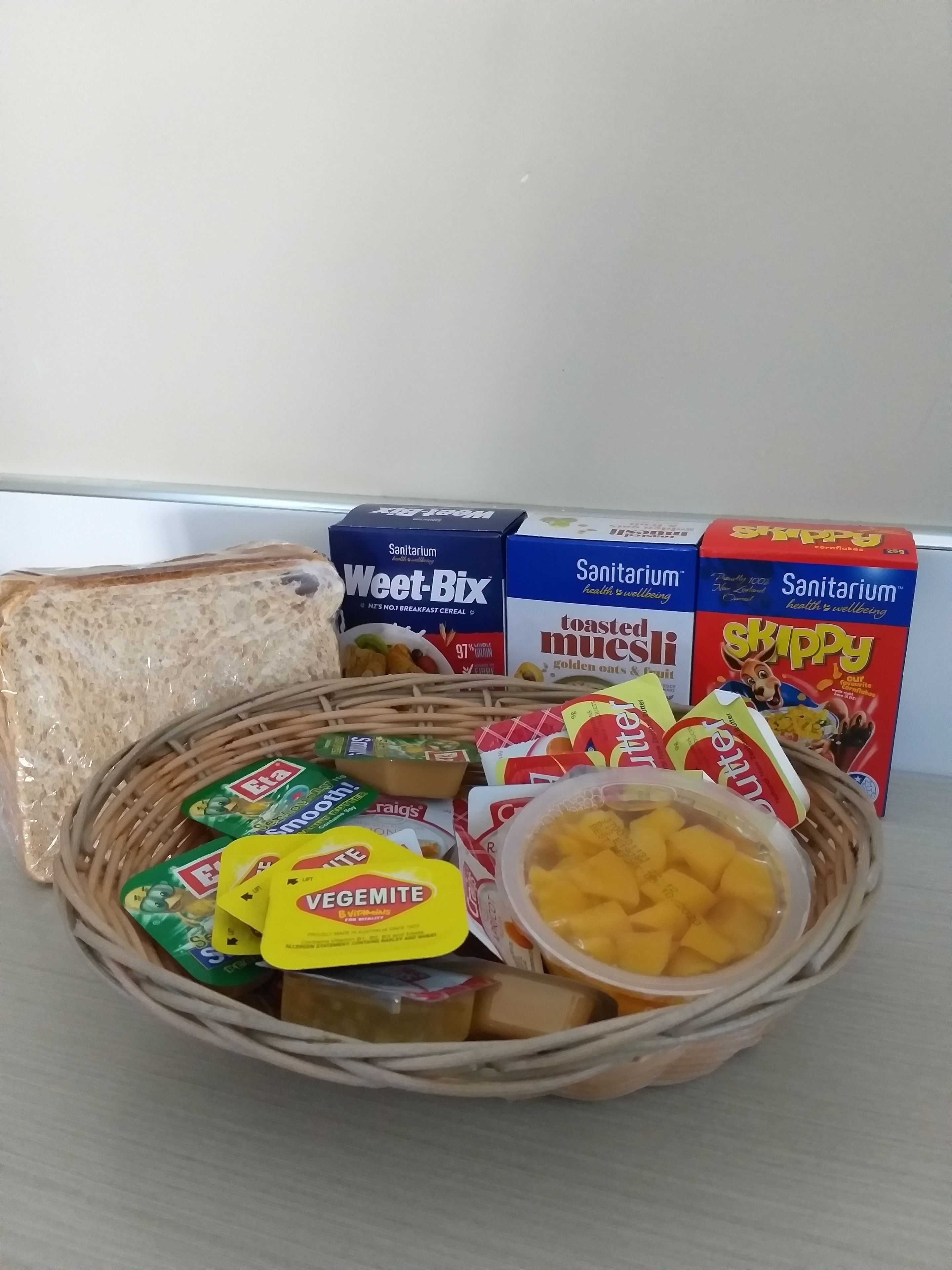 Una cesta con distintos productos de desayuno, como pan, cereales y fruta.