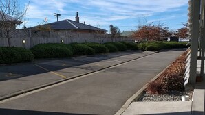 A parking lot with a clear sky, a building with a sloped roof, and a fence with satellite dishes. - Tinwald Motels (Ashburton)