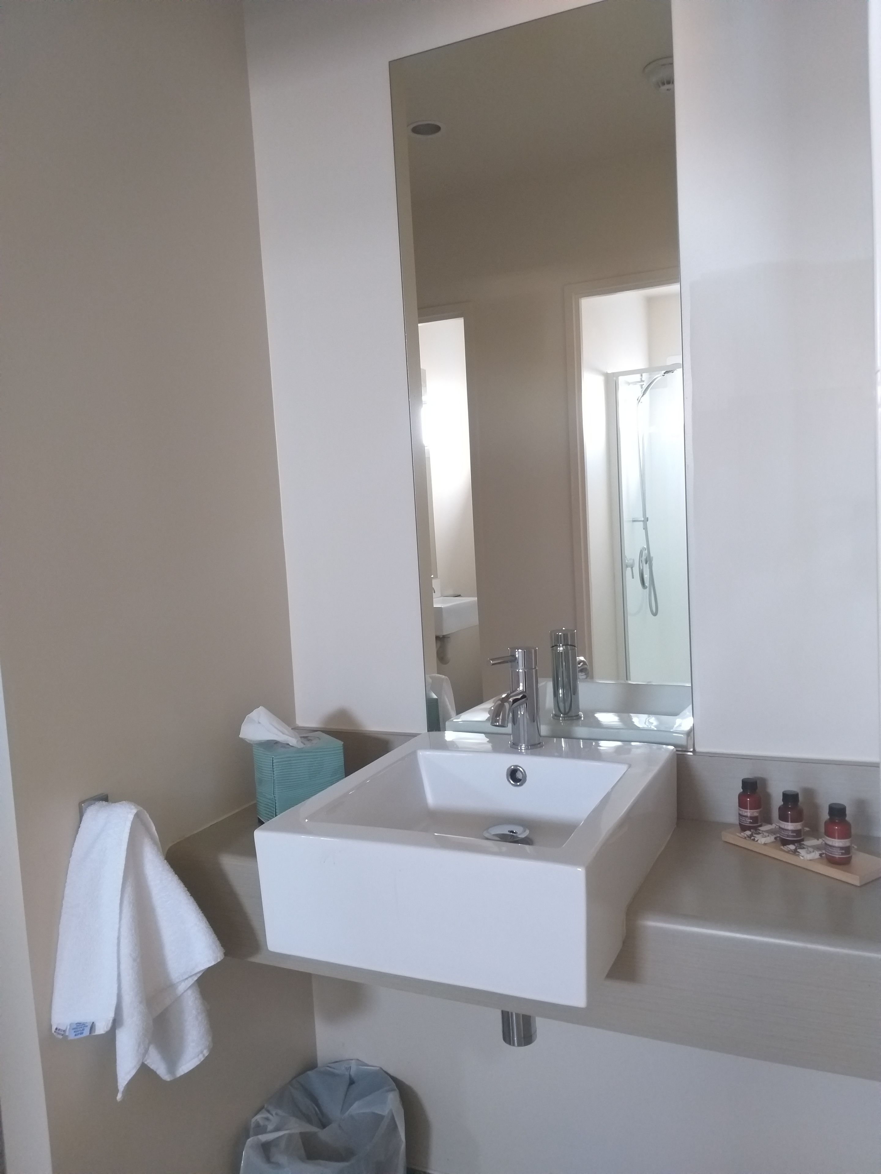 A bathroom with a large mirror, a white sink, and a towel hanging on the wall.
