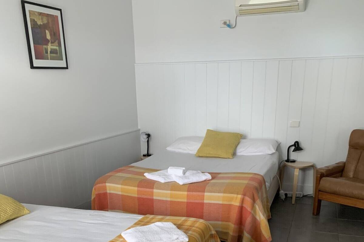 Habitación de hotel con dos camas, cada una con una colcha de cuadros diferente, una mesita con una lámpara y una silla.