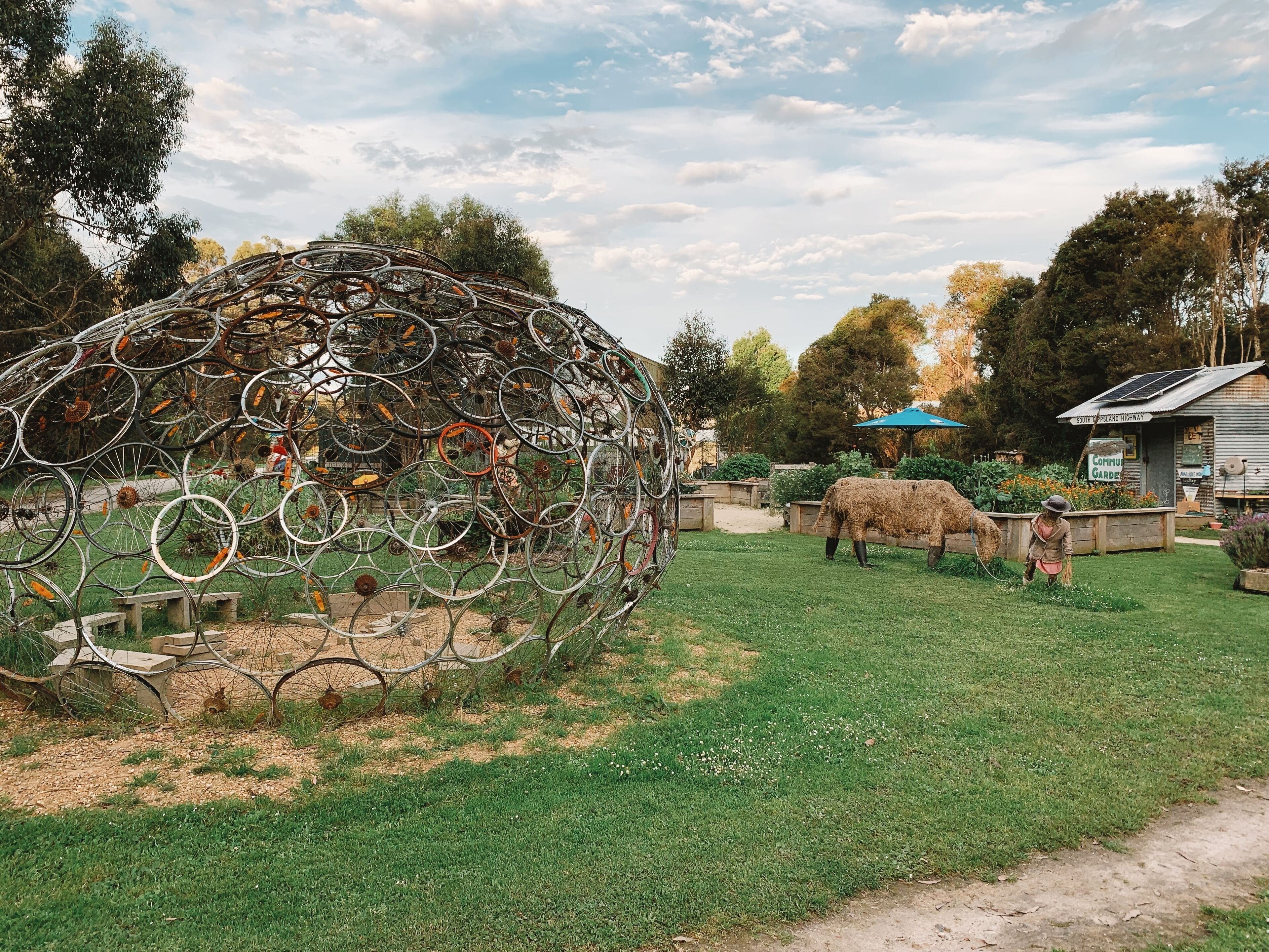 Una escultura de bicicletas en un jardín, con un pequeño edificio al fondo que dice "South Coast Highway".