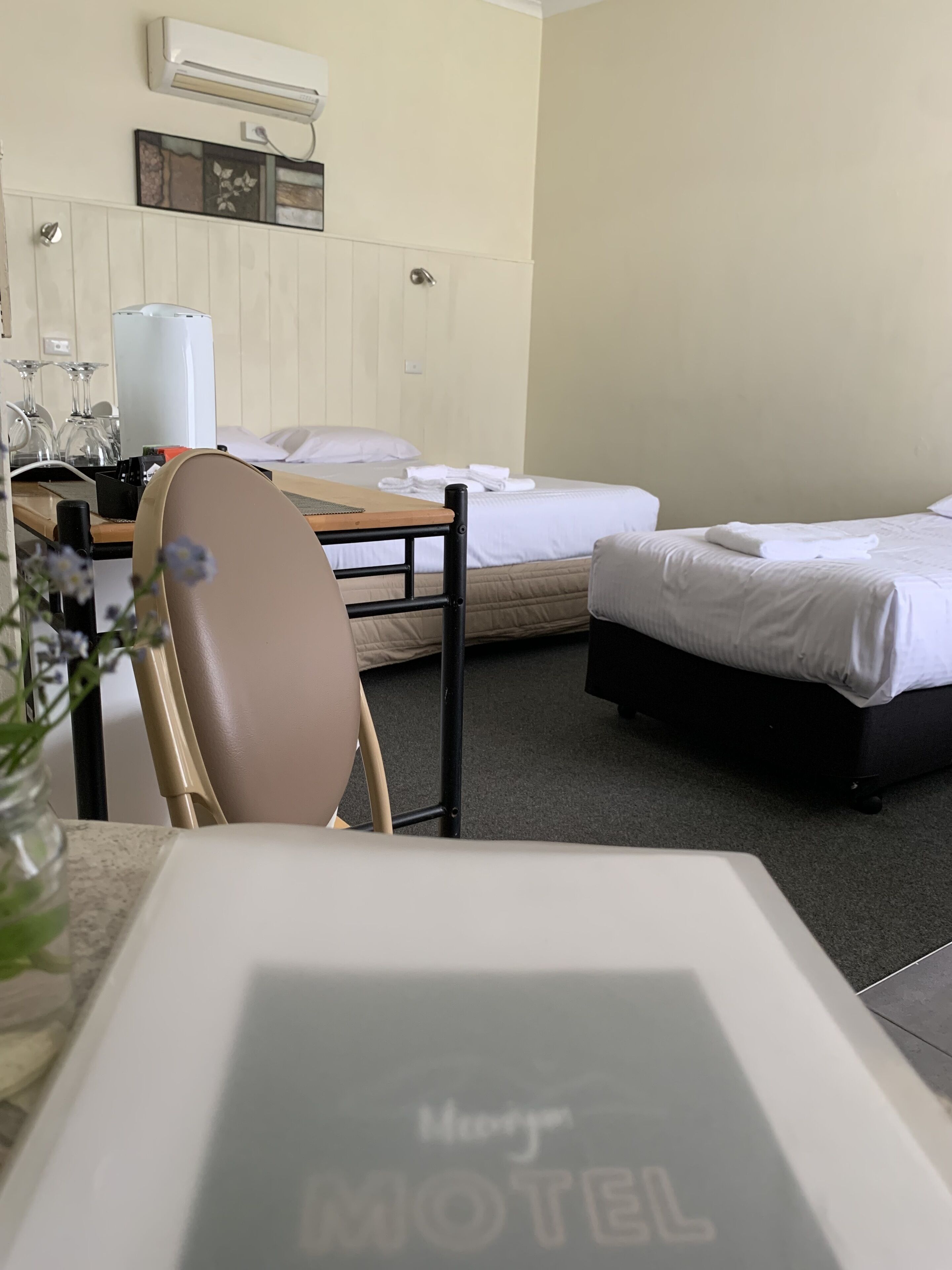 A motel room with two beds, a desk with a chair, and a small table with a vase of flowers.