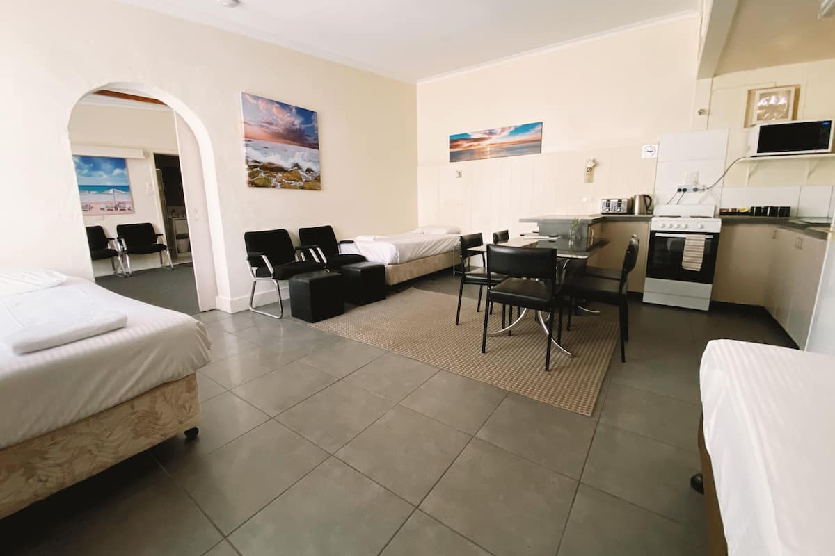 Habitación de hotel con cama, escritorio con silla, kitchenette y baño visible a través de un arco.