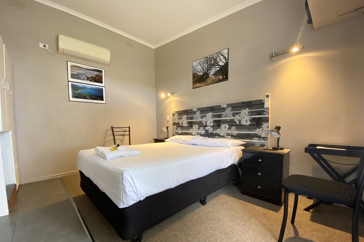 A bedroom with a bed, a chair, a desk, and a wall-mounted air conditioner.