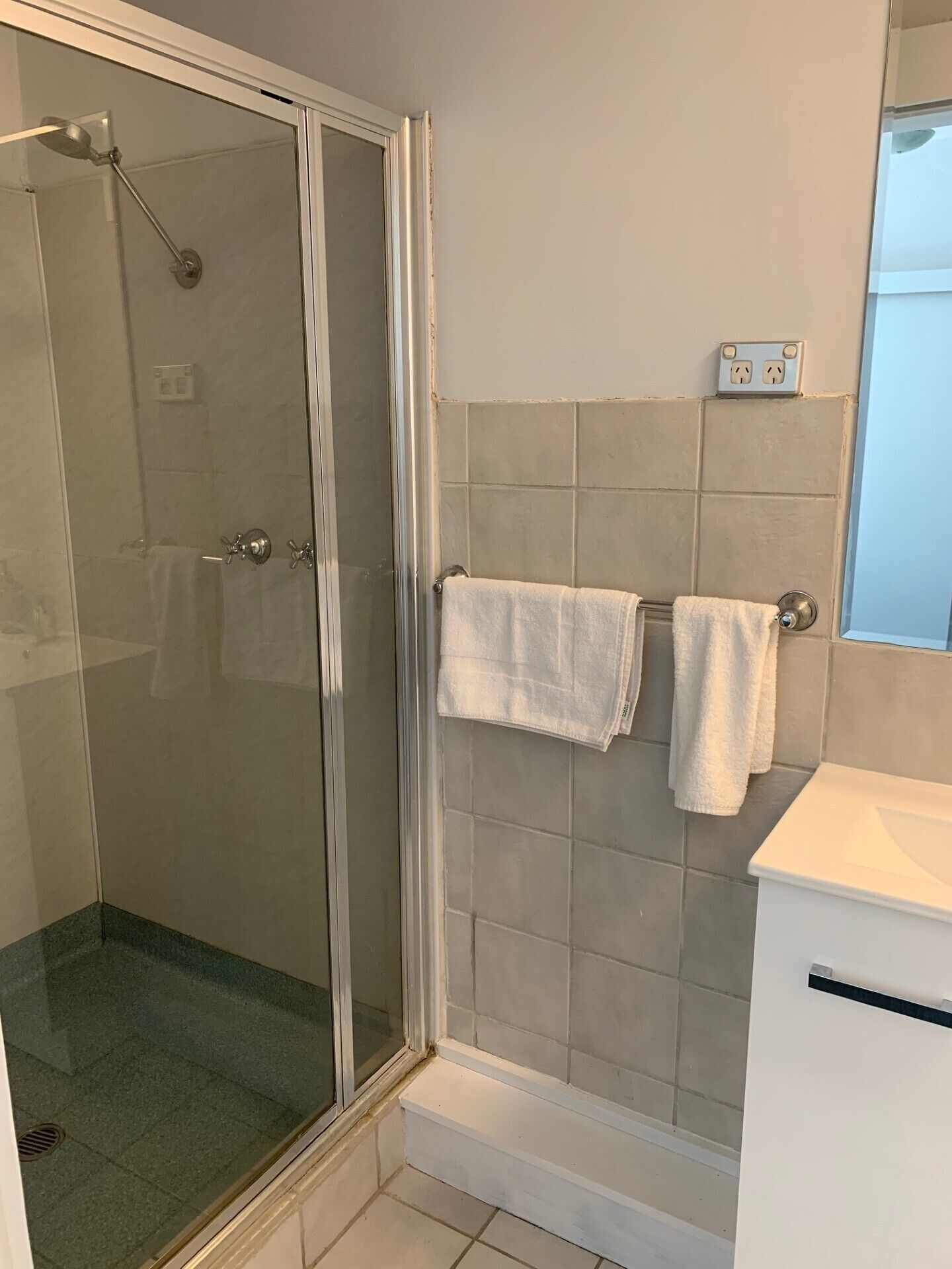 A bathroom with a glass shower enclosure, a white sink, and a mirror above it.
