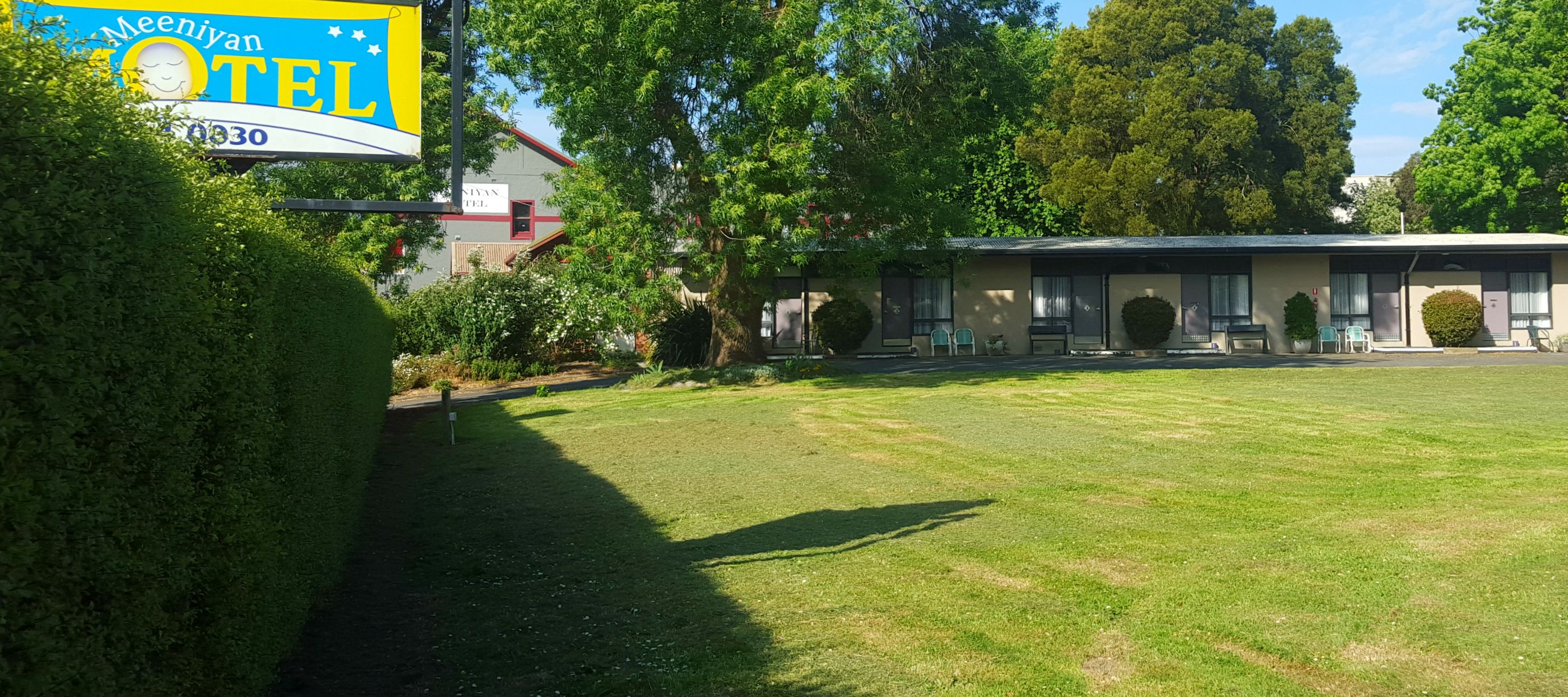 A motel with a signboard, a lawn, and a building with multiple rooms.
