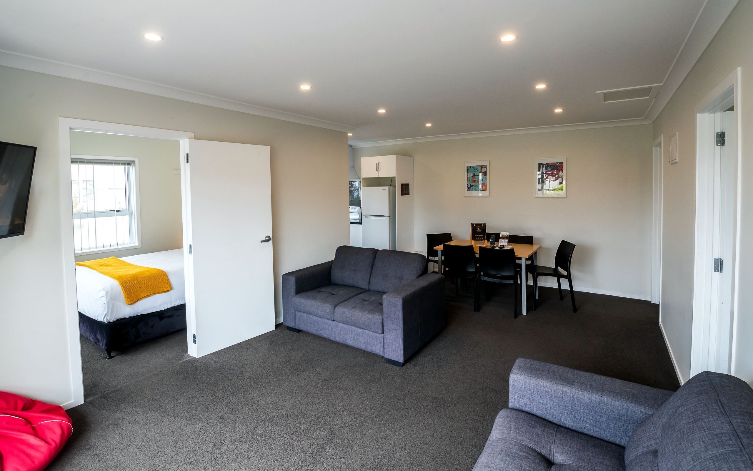 A compact living space with a sofa, a bed, a dining table with chairs, and a kitchen area.