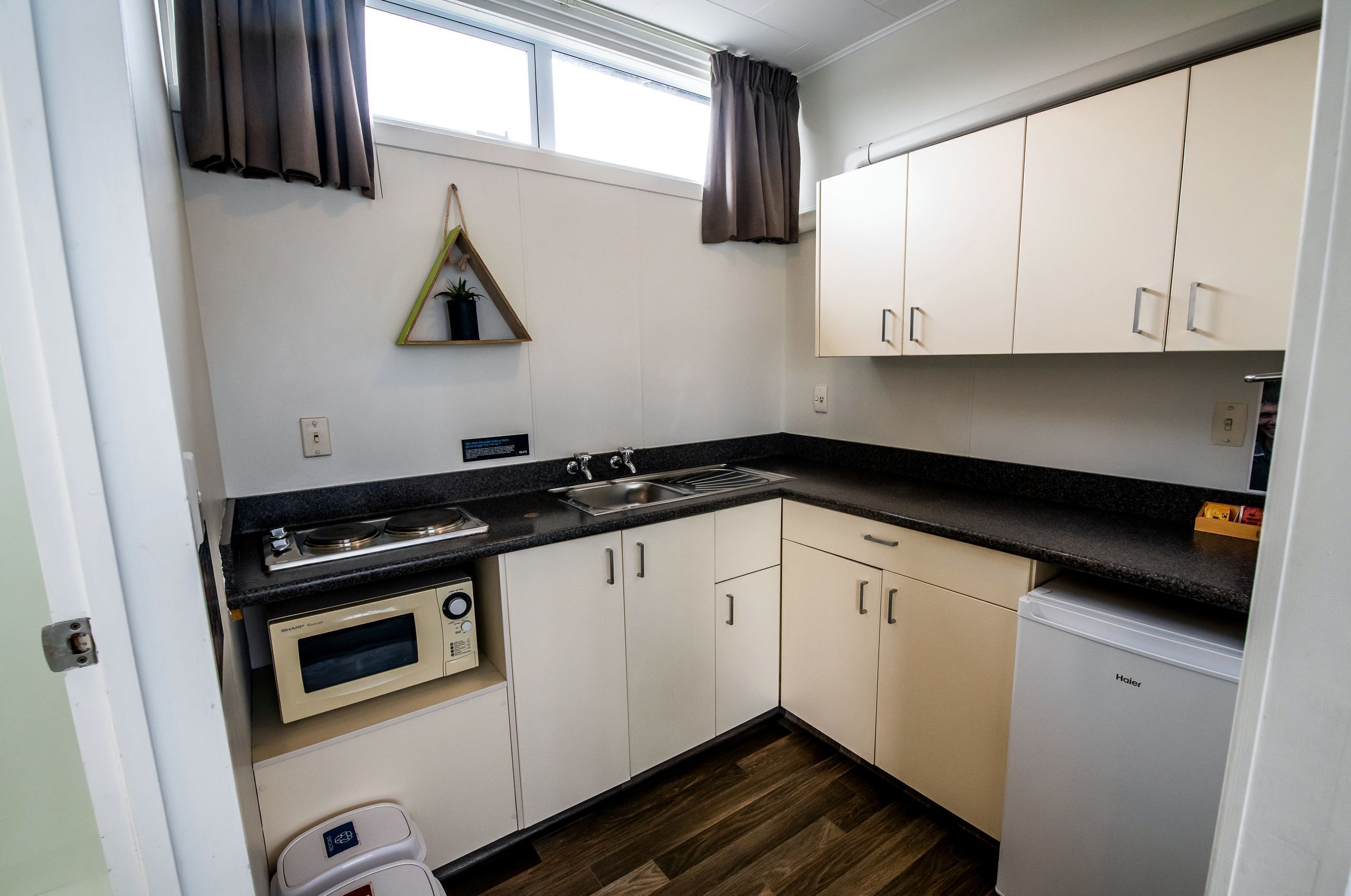 Una cocina compacta con armarios blancos, una encimera negra, un microondas, un lavabo y un refrigerador.