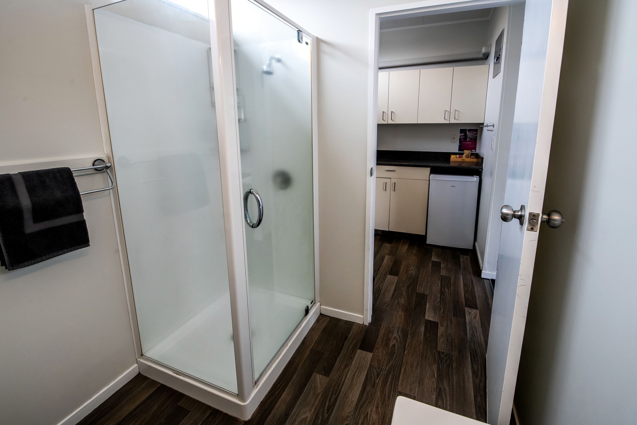 A modern bathroom with a glass shower enclosure, a white sink, and a wooden floor.