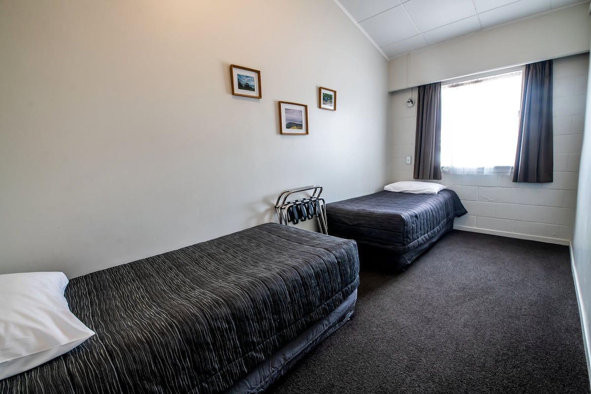 Una habitación de hotel con dos camas individuales, un pequeño rincón de descanso y una ventana con cortinas.