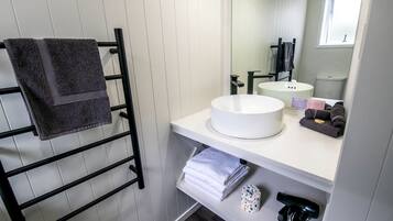 A bathroom with a white sink, a towel rack with folded towels, a mirror, and a window.