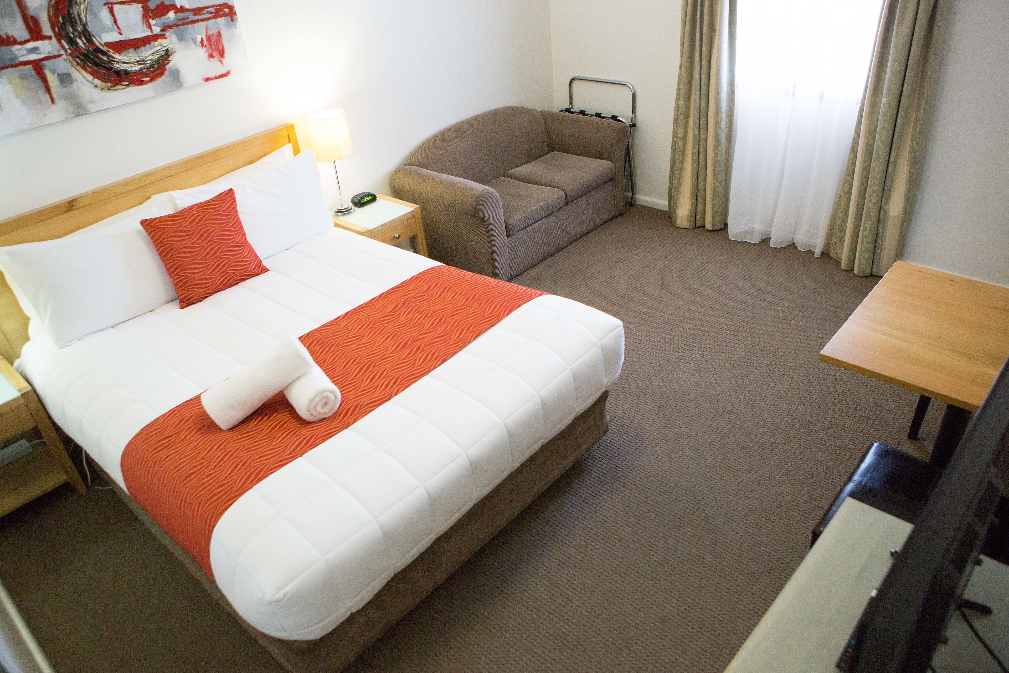 A hotel room with a large bed, a sofa, a desk, and a chair.