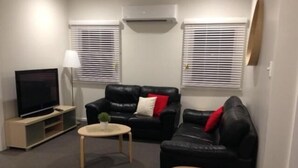 A living room with a TV, two black leather sofas, a small wooden coffee table, and a white lamp. - Colonial Lodge Motor Inn Yass (Yass)