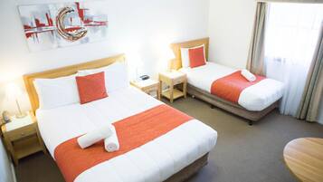 A hotel room with two beds, each with white and orange bedding, a nightstand with a lamp, and a painting on the wall.