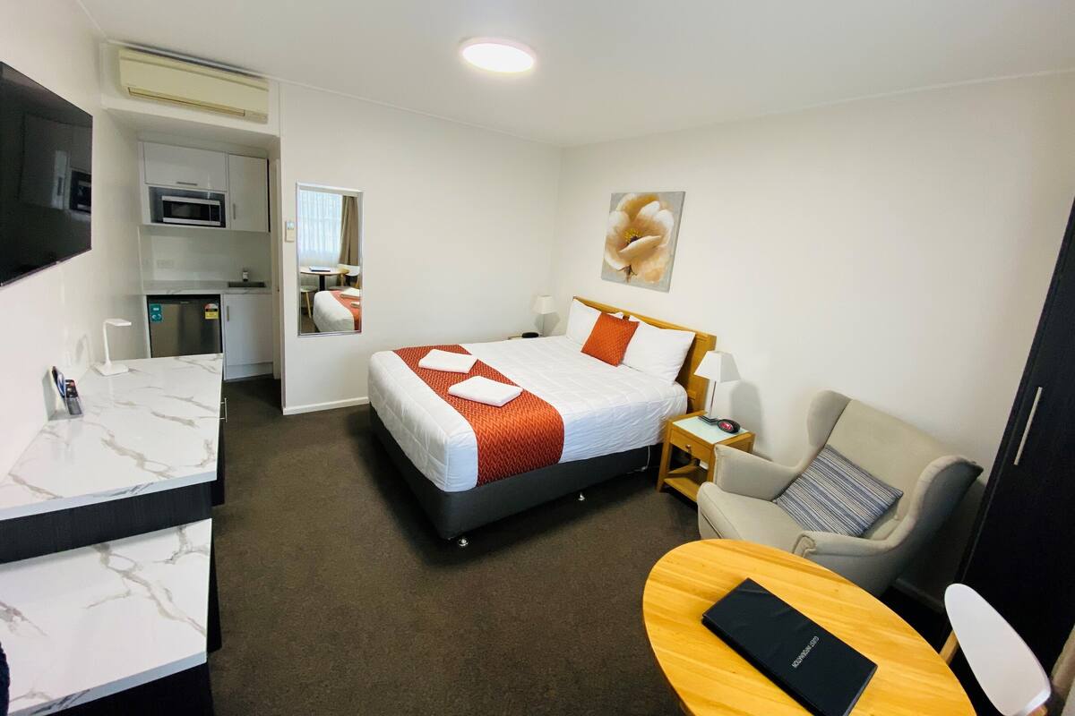 A hotel room with a bed, a desk, a chair, a TV, and a microwave.