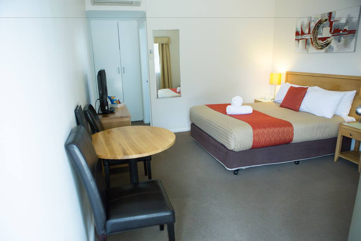 A hotel room with a bed, a desk, a chair, a television, and a mirror.