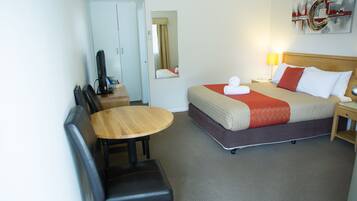 Quarto de hotel com cama, escrivaninha, cadeira, televisão e espelho.