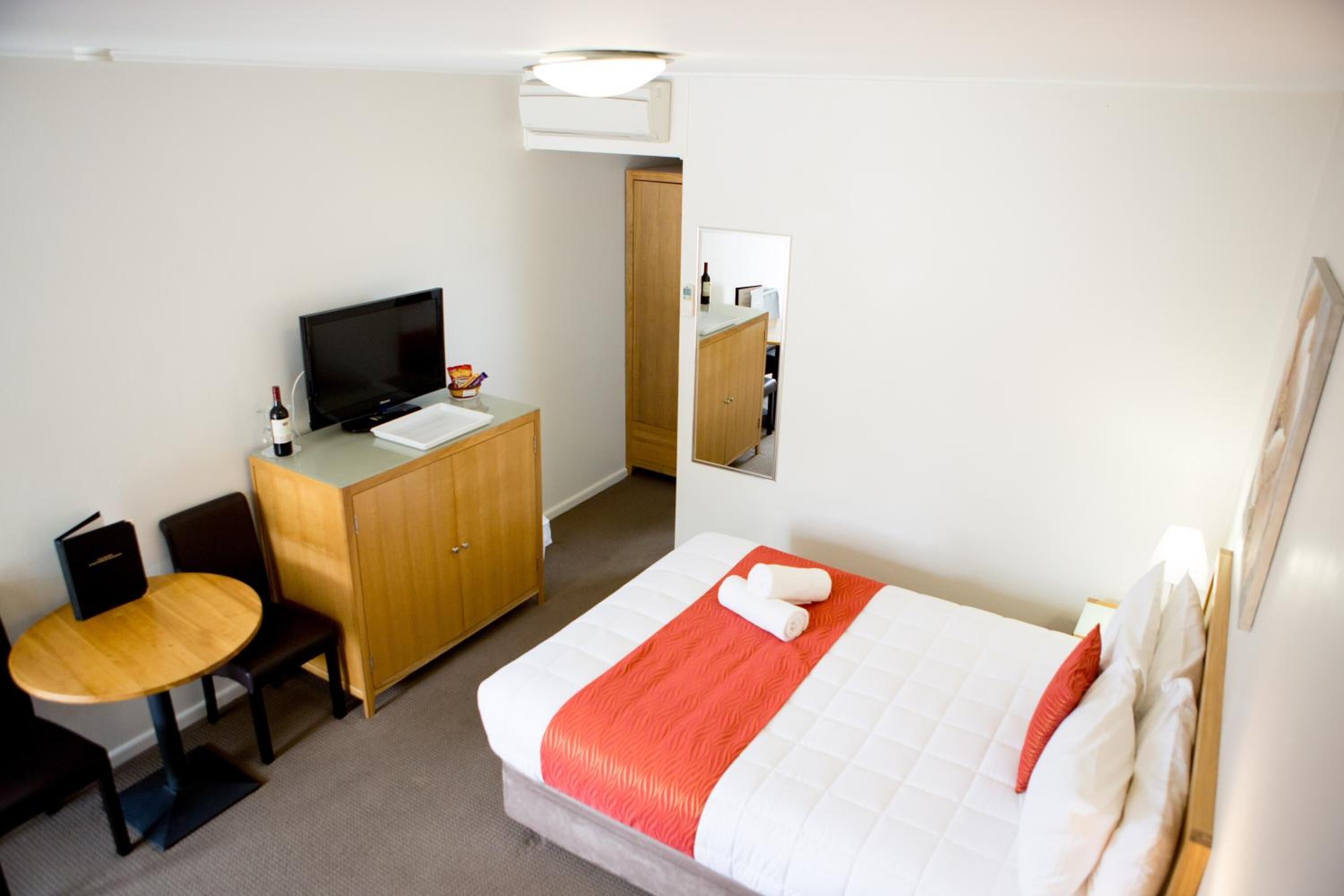 Ein Hotelzimmer mit einem Bett, einem Schreibtisch mit Computer, einem Sessel, einem kleinen Tisch und einem Spiegel.
