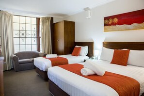 Two single beds with white linens and orange accents, a grey armchair, and a wardrobe.