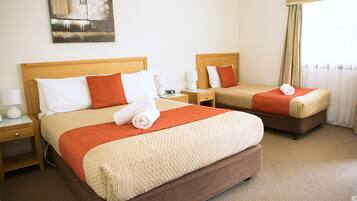 Quarto de hotel com duas camas, cada uma com cabeceira de madeira, almofadas brancas e laranja e um cobertor bege. Há mesas de cabeceira com abajures e um quadro na parede.